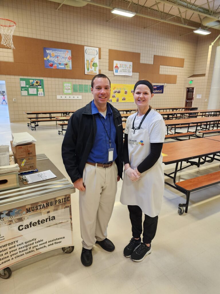 Andrew with Cafeteria Staff at School Visit Andrew standing with a cafeteria staff member inside a school cafeteria.