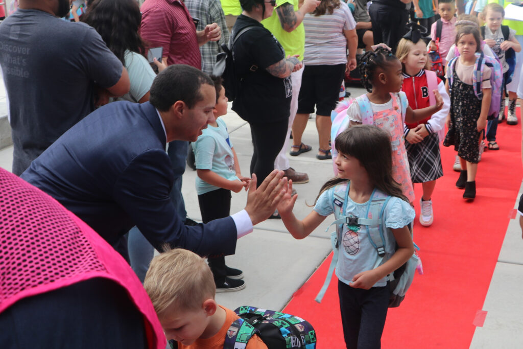 Red Carpet First Day Welcome – Andrew with Students Andrew high-fiving a young student on the red carpet during a first-day-of-school welcome event.”