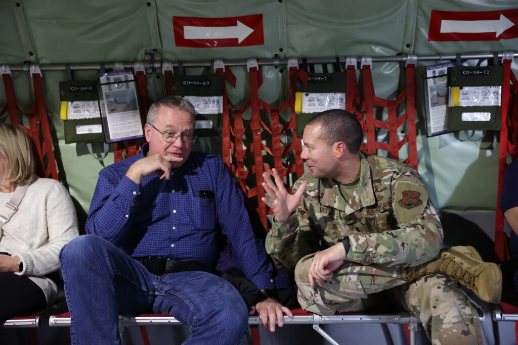 Andrew Speaking with Community Member on Military Aircraft Andrew in military uniform talking with a man while seated inside a military aircraft.