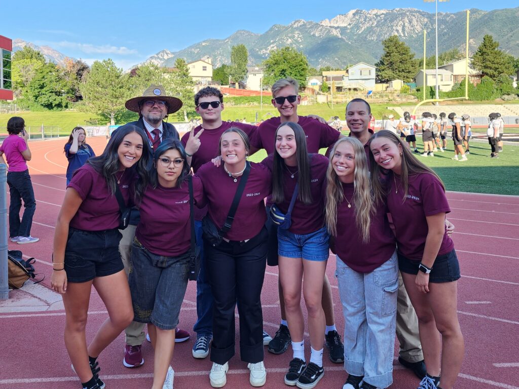 Andrew with Jordan High Students on Track Field Group of high school students and an adult standing together on a track field with mountains in the background.
