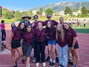 Andrew with Jordan High Students on Track Field Group of high school students and an adult standing together on a track field with mountains in the background.