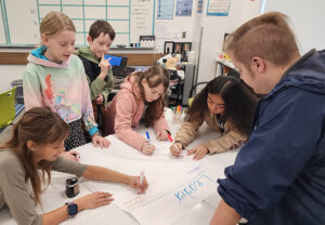 Supportive School Environment A group of upper-elementary students collaborate on a classroom activity while an adult supports them.